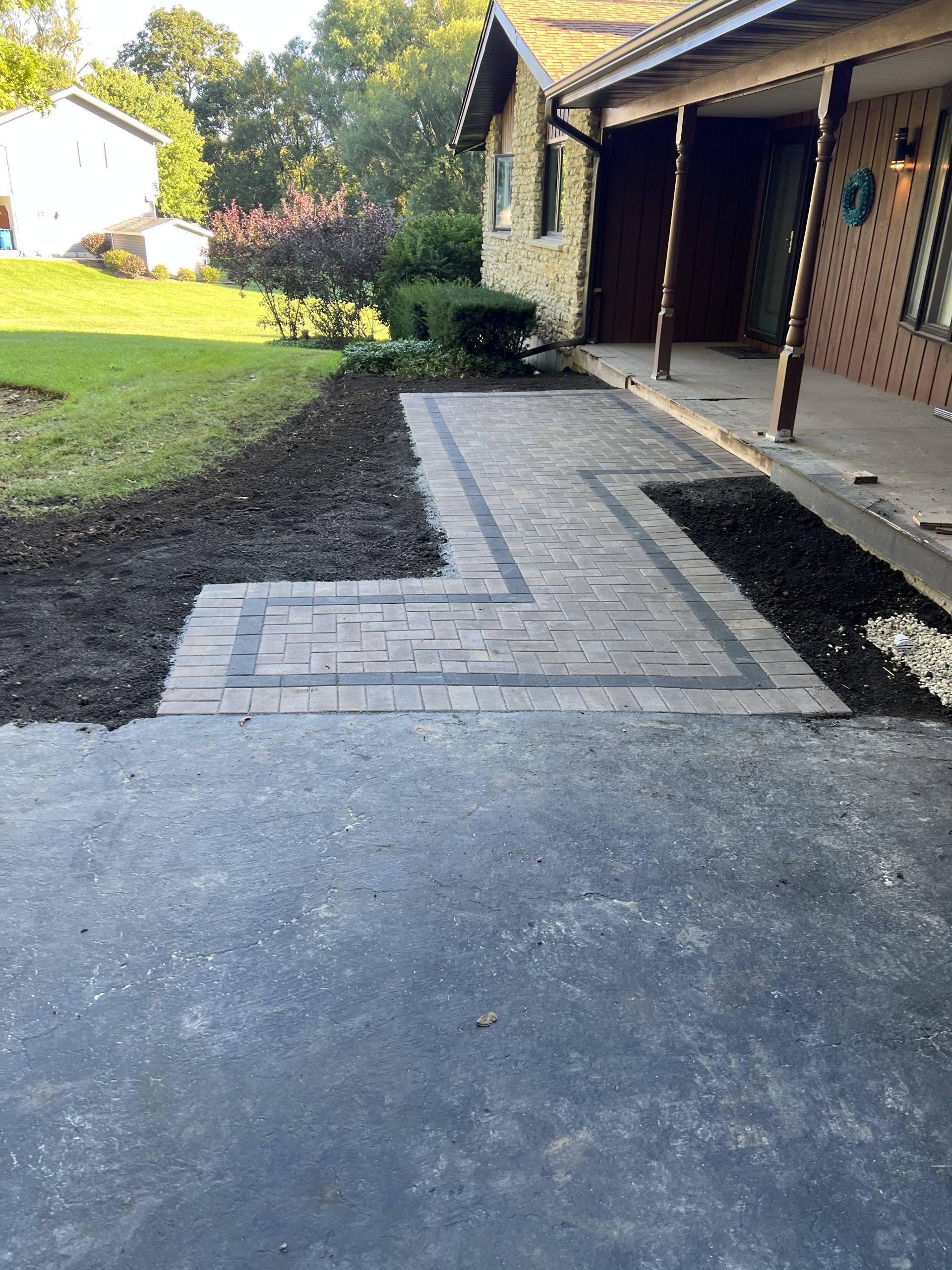 Brick pathway leading to a house with a porch, set on a driveway and grass lawn.