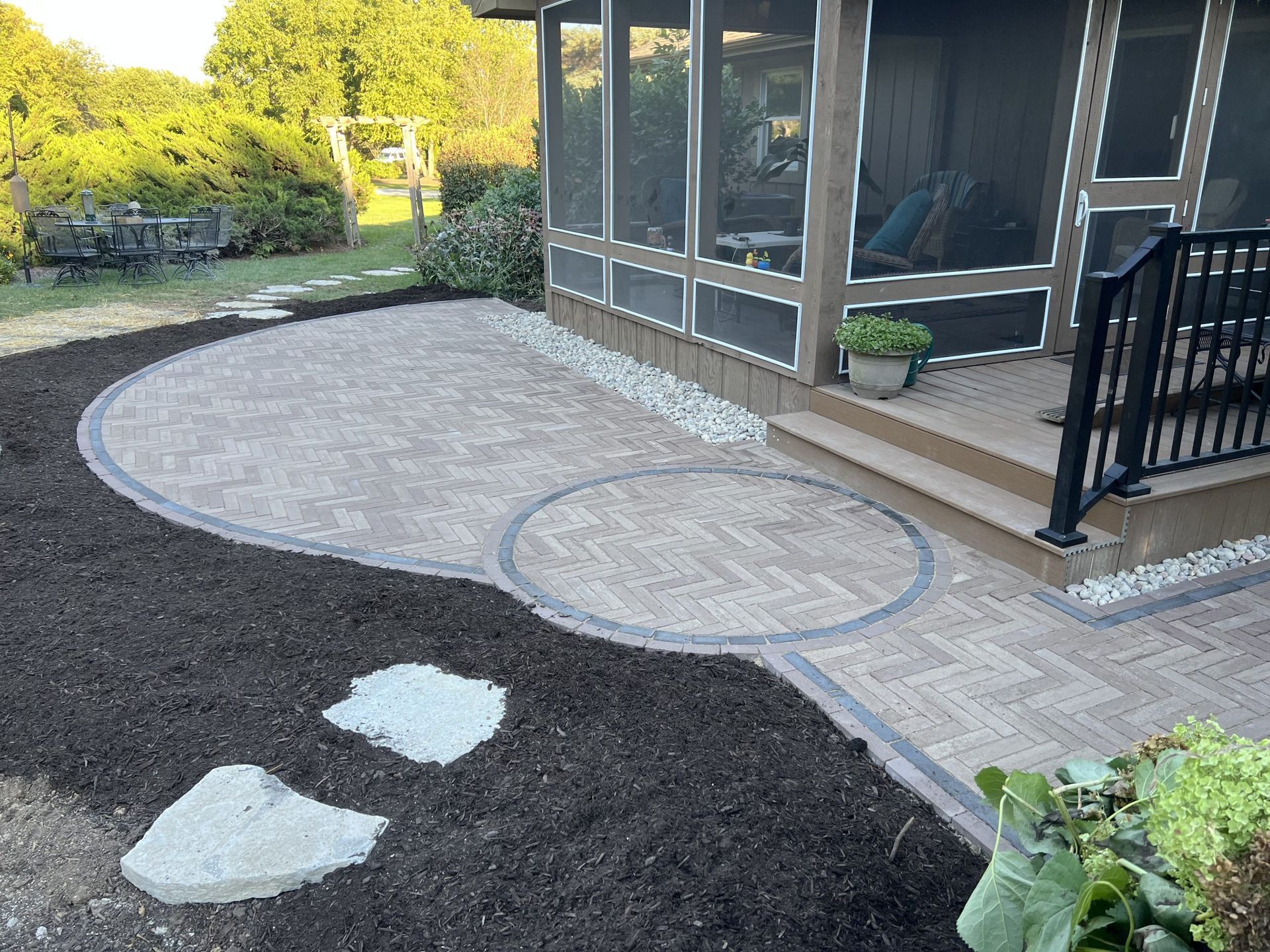 Brick patio with screened porch, stepping stones, and dark mulch.