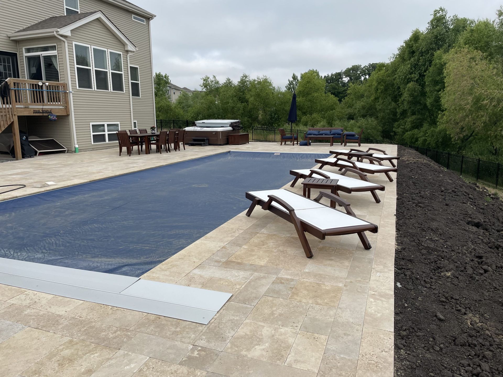 Backyard pool with a blue cover, lounge chairs, and a house.
