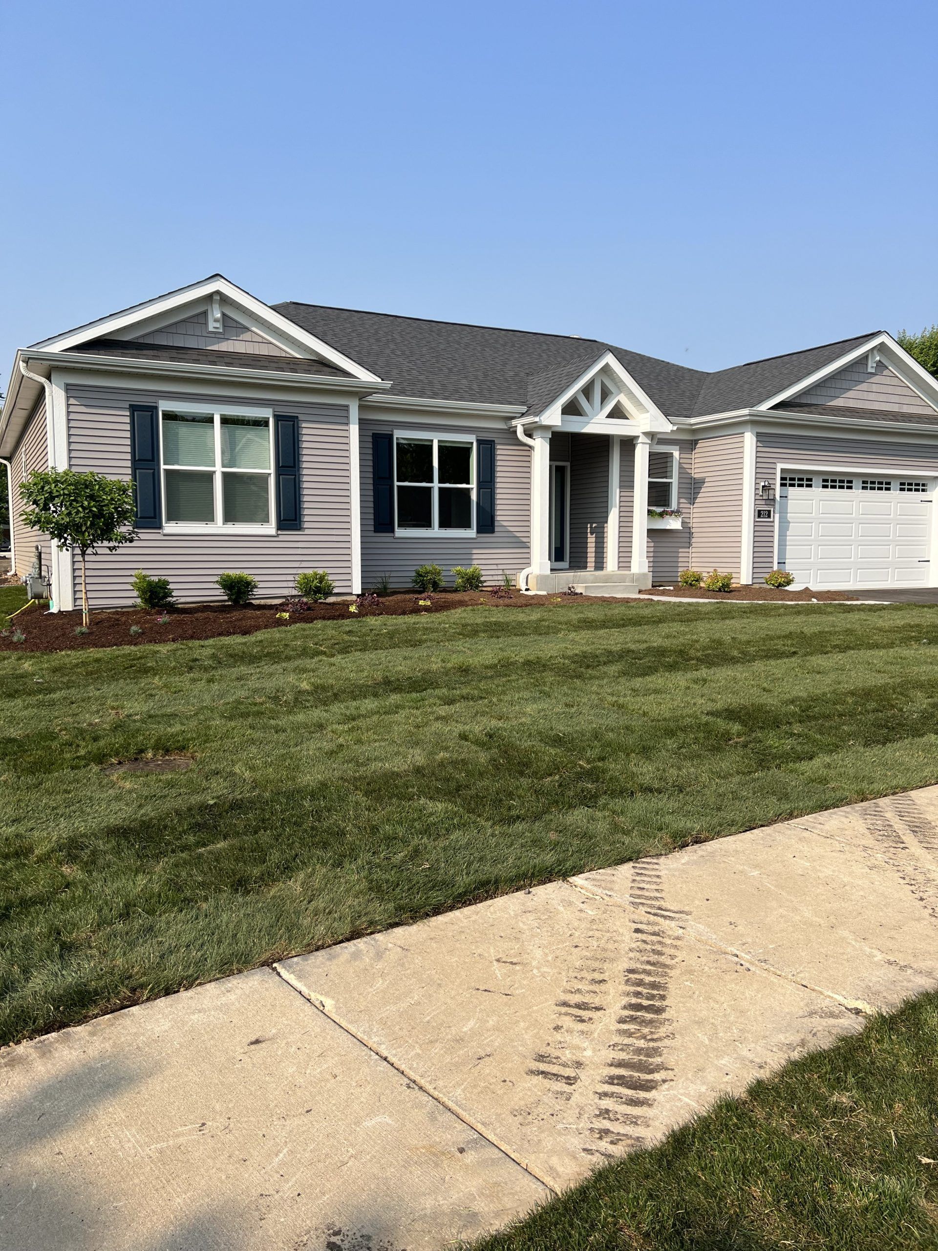 Light gray house with blue shutters, a dark gray roof, and a green lawn.
