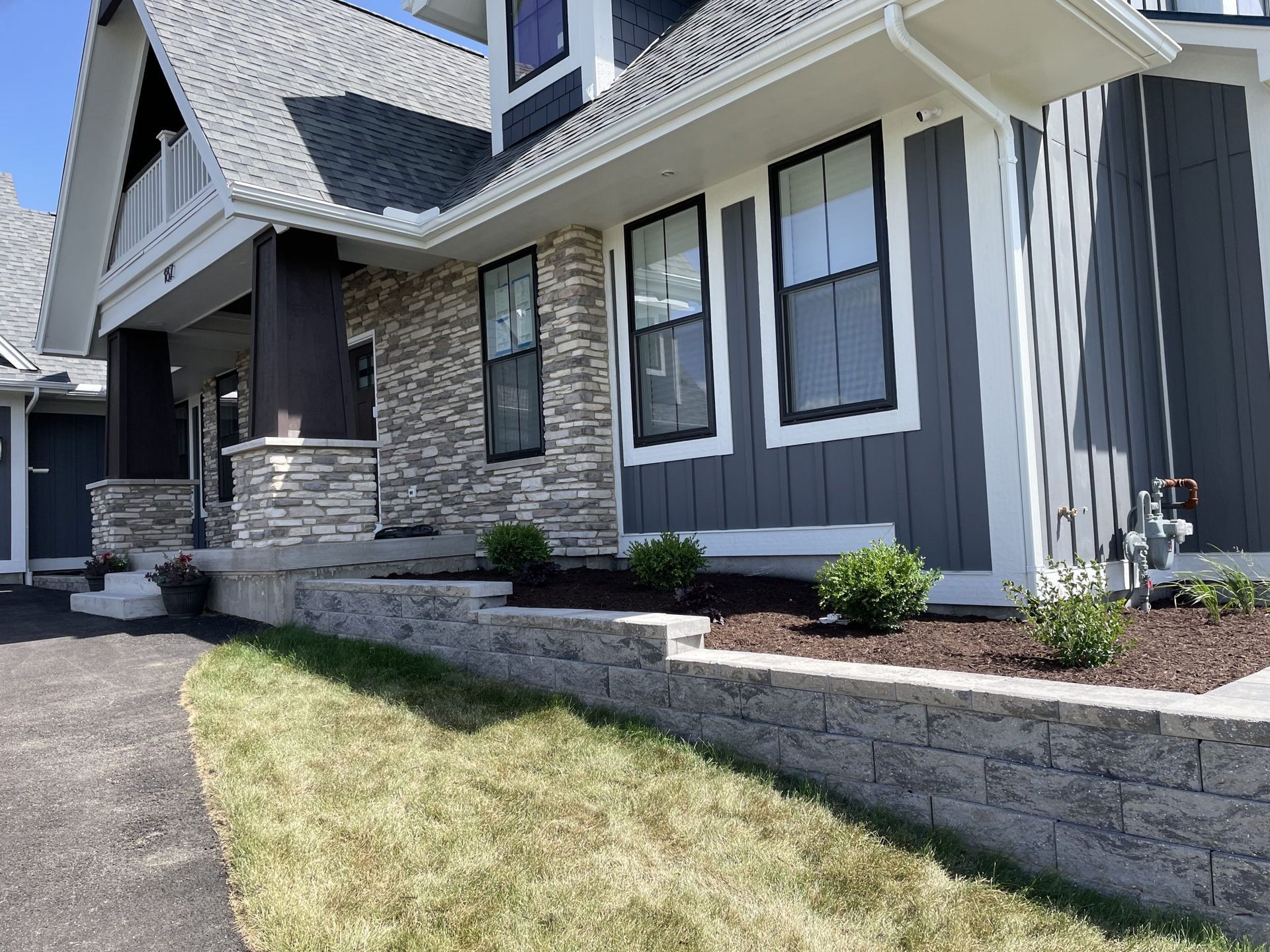 Modern house with gray siding, stone facade, retaining wall, and green lawn.