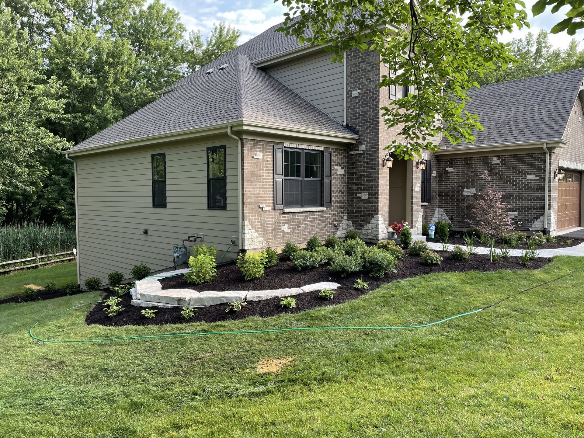 House with stone accents, lush landscaping, and green grass lawn.