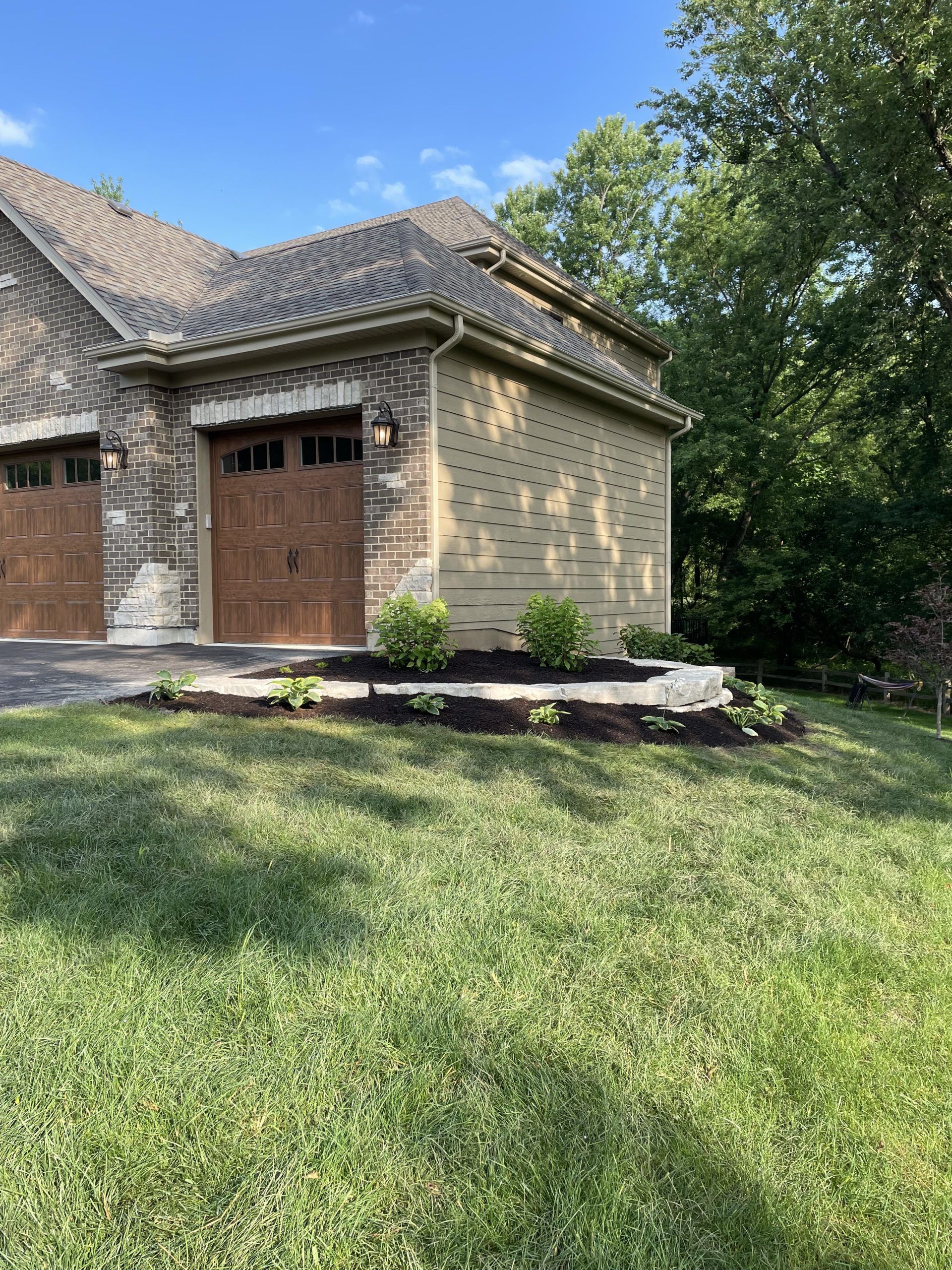 Garage with brown doors and a small garden bed in front, on a sunny day.