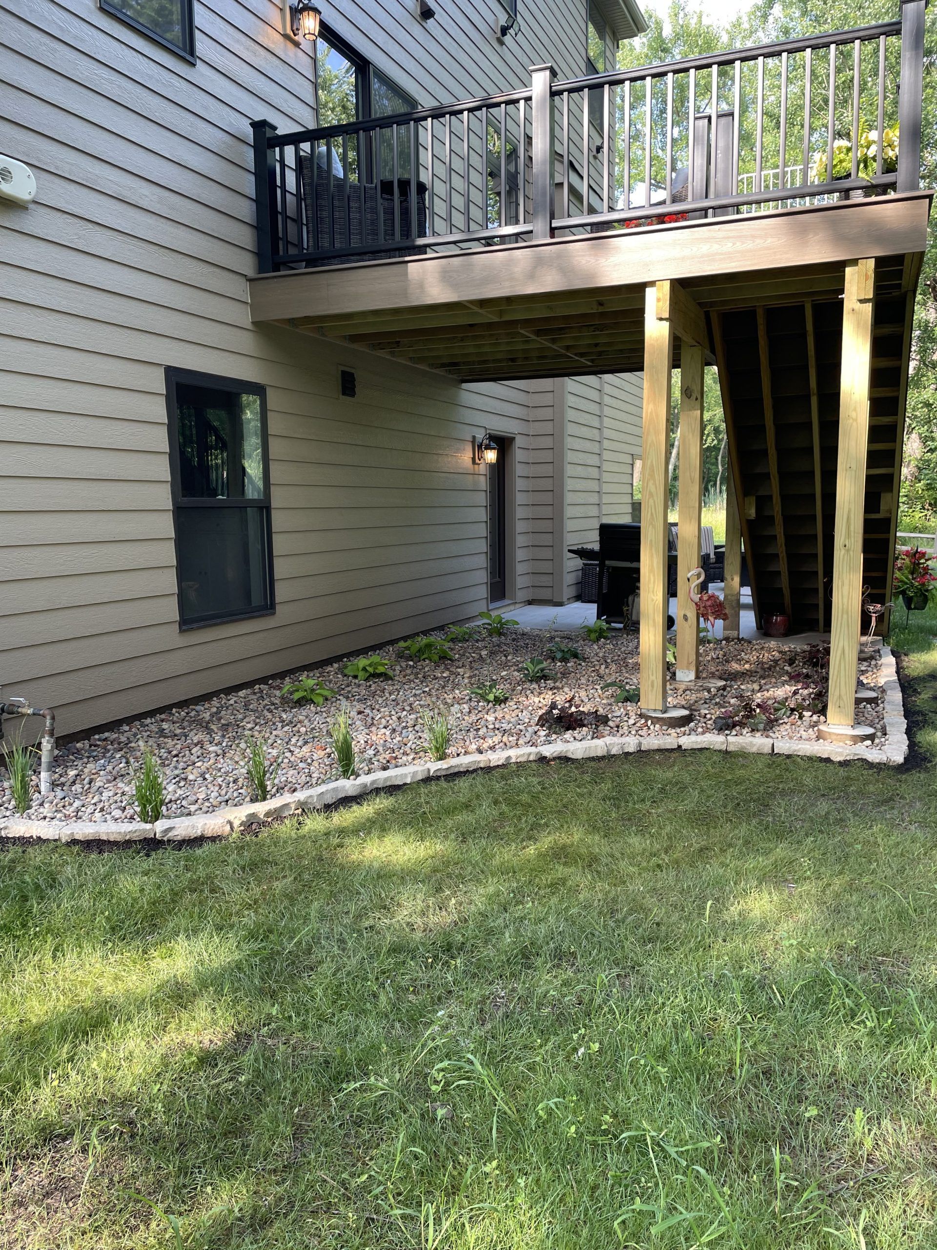 A house with a raised deck, a stone-lined garden, and wooden posts supporting the deck.