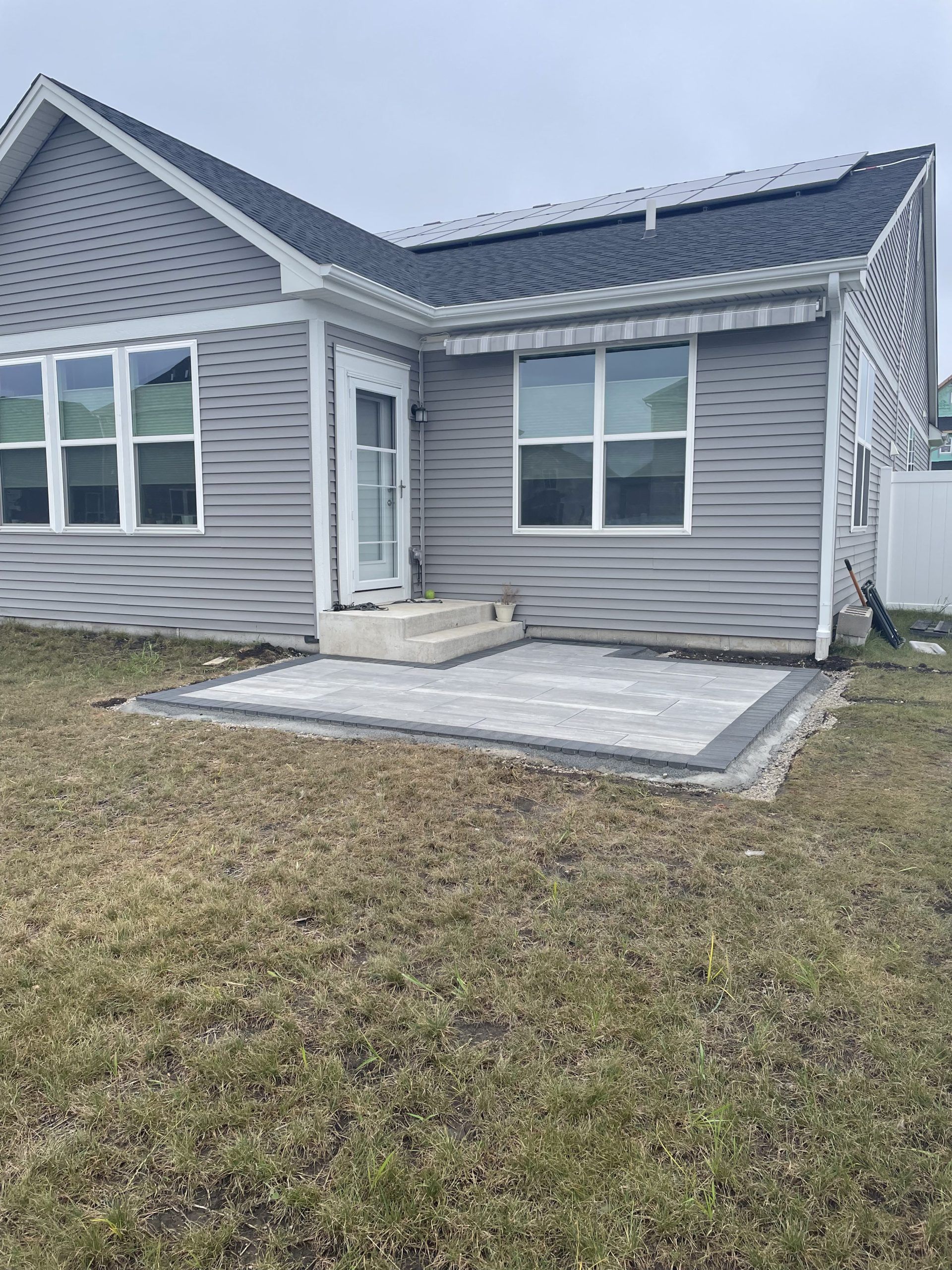 Patio with gray pavers outside a house with gray siding and a door.
