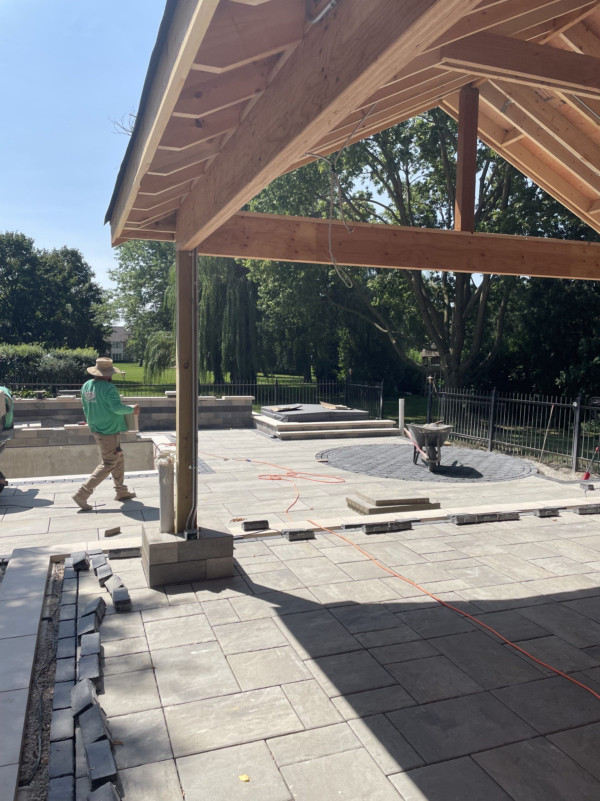 Construction of an outdoor structure: wooden frame, patio pavers, worker, trees in background.