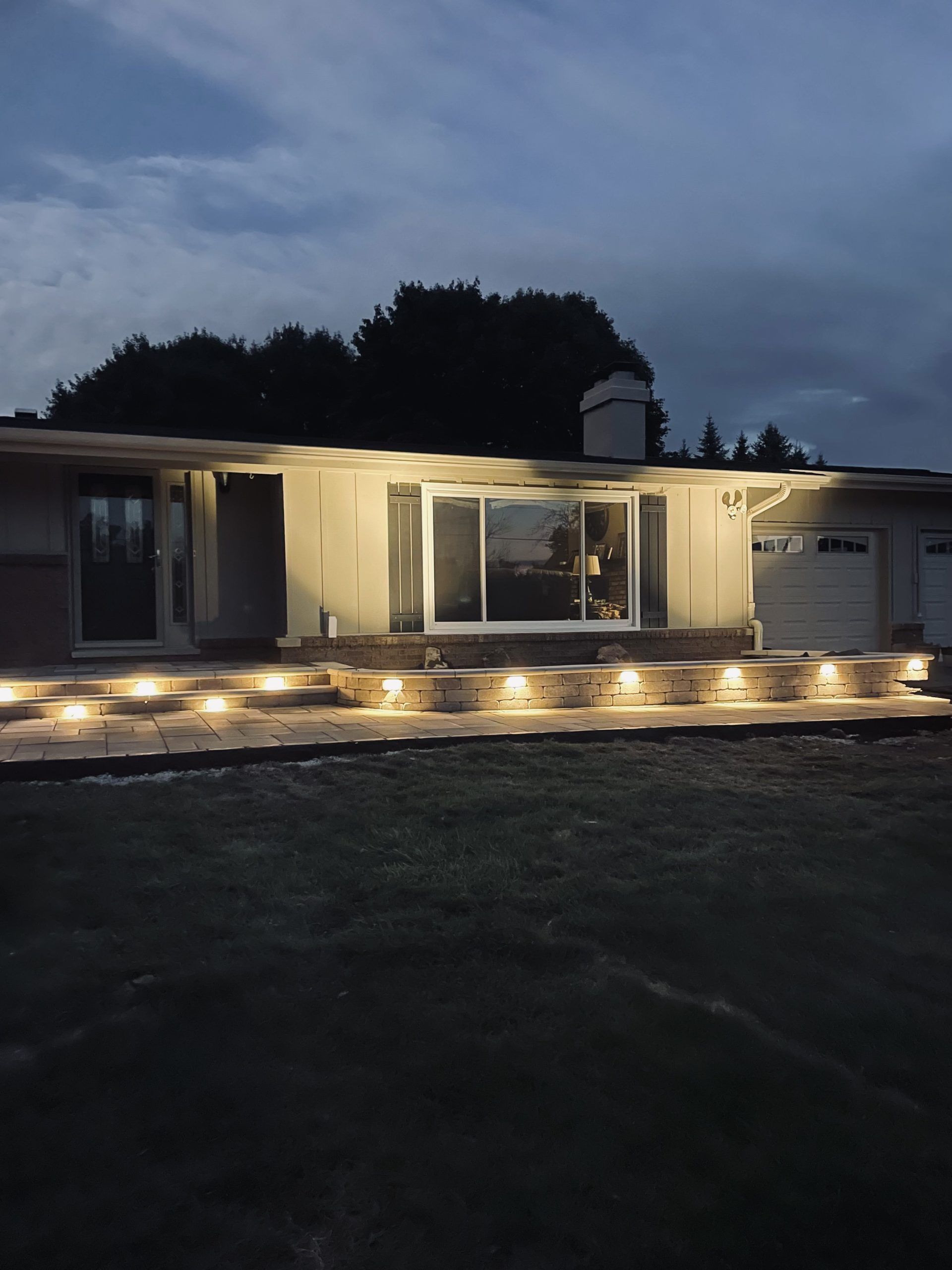 Night view of a house with lit pathway steps. The house has a garage and large sliding glass doors.