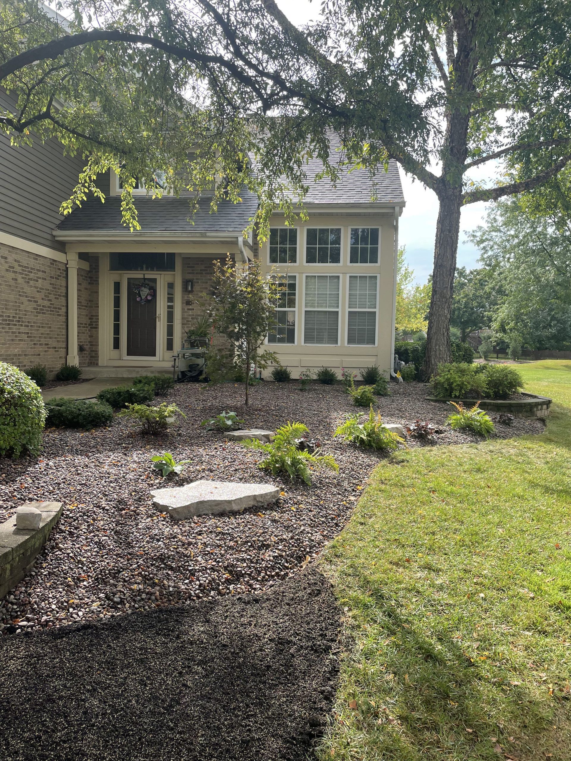 House exterior with landscaping: a porch, windows, and mulch-covered garden with stepping stones and green shrubs.