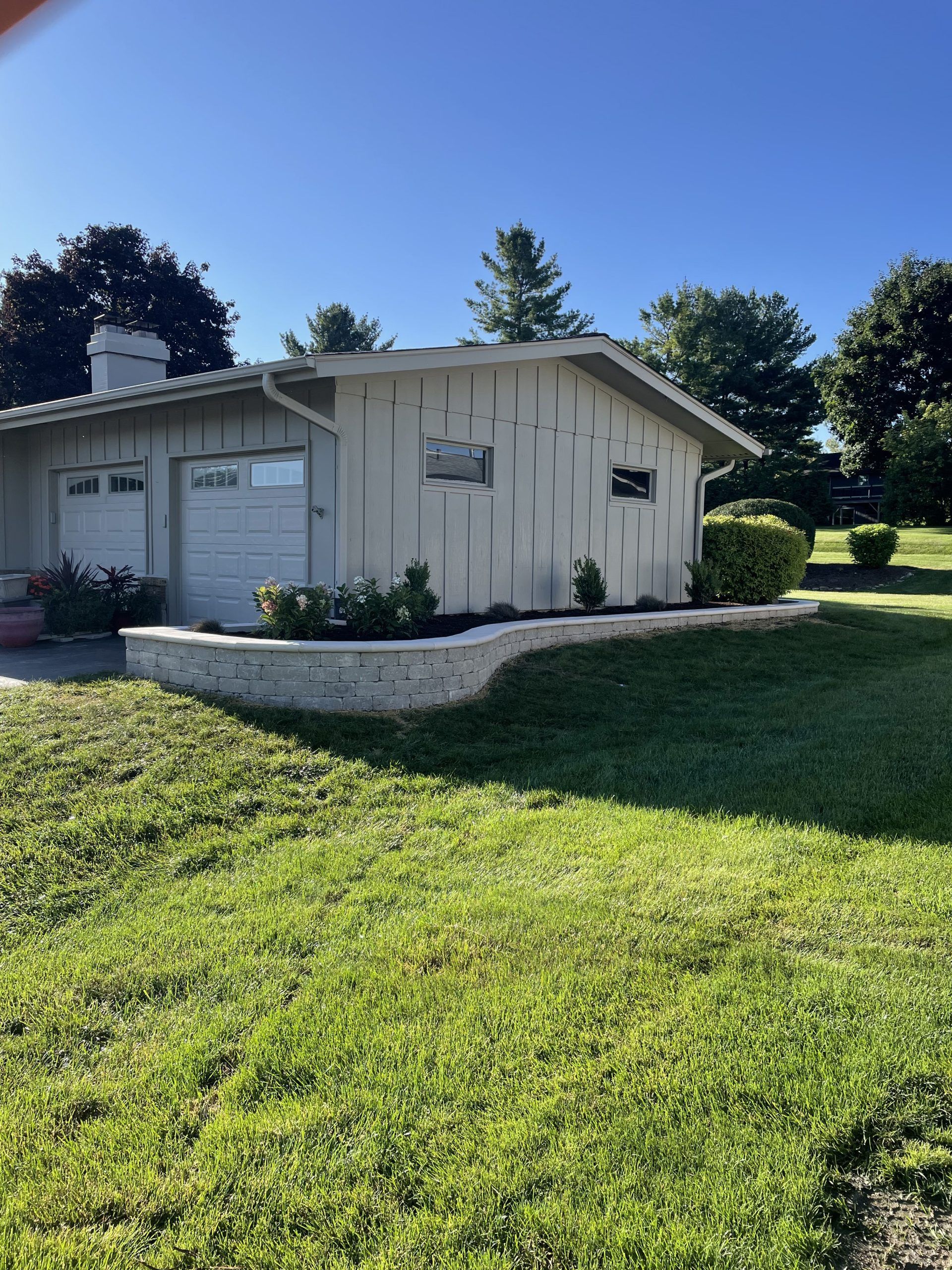 Garage with two doors and a curved retaining wall in front, on a sunny day.