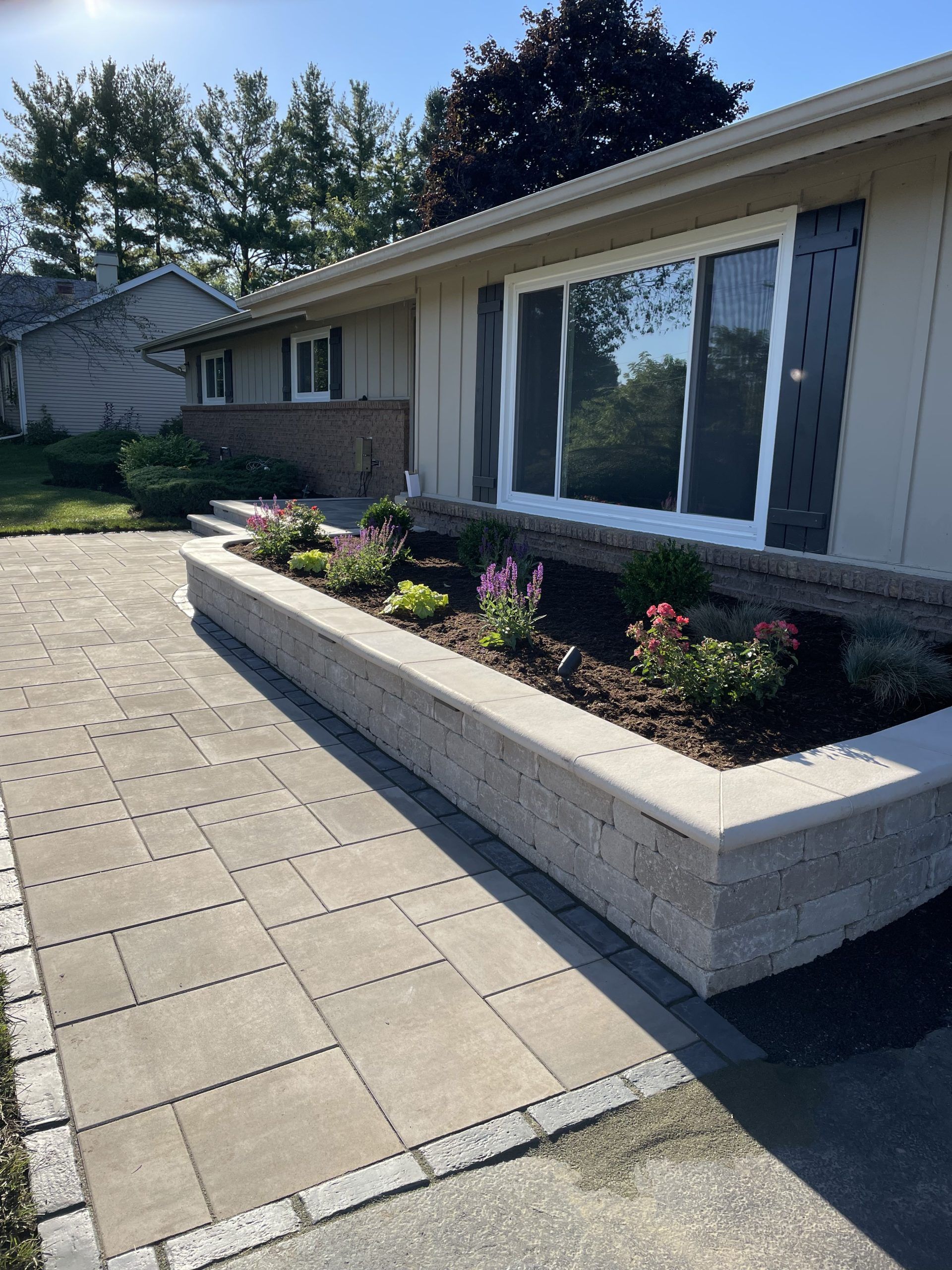Stone walkway leading to a house with a raised flower bed filled with plants.