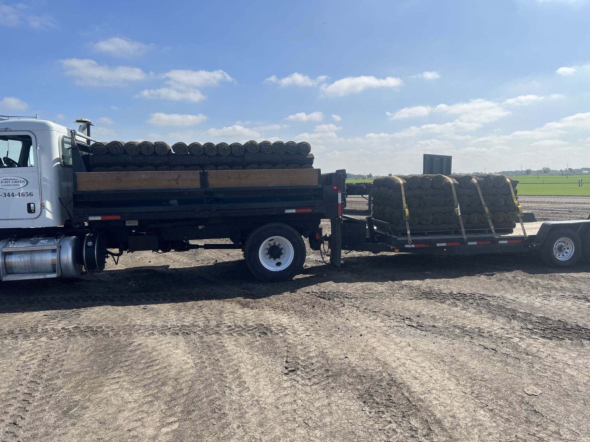 Truck and trailer loaded with rolls of sod on a dirt road under a cloudy sky.