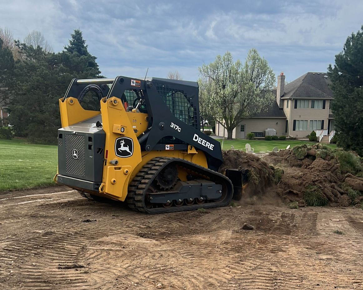 John Deere skid steer compacting gravel in a field.