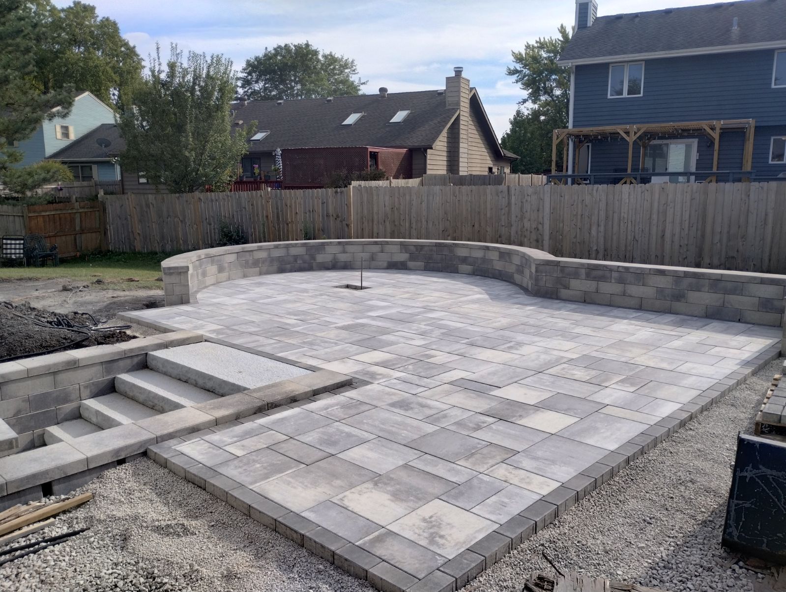 Newly constructed patio with gray pavers and retaining wall; steps lead up to the patio.