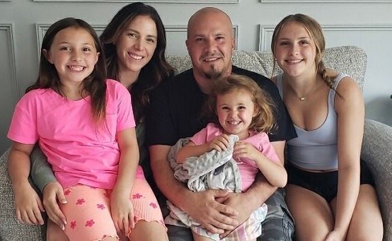 Family of five smiling, sitting together on a light-colored couch.