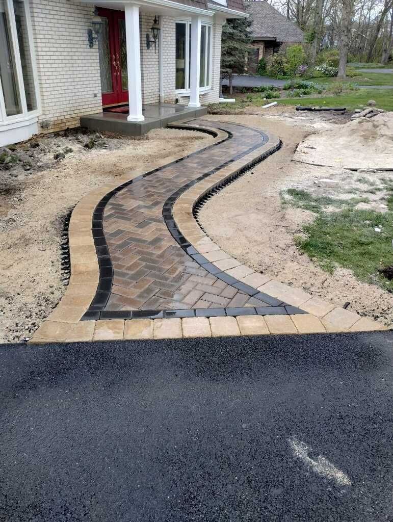 Brick pathway leading to a house with a red door, winding through a yard.