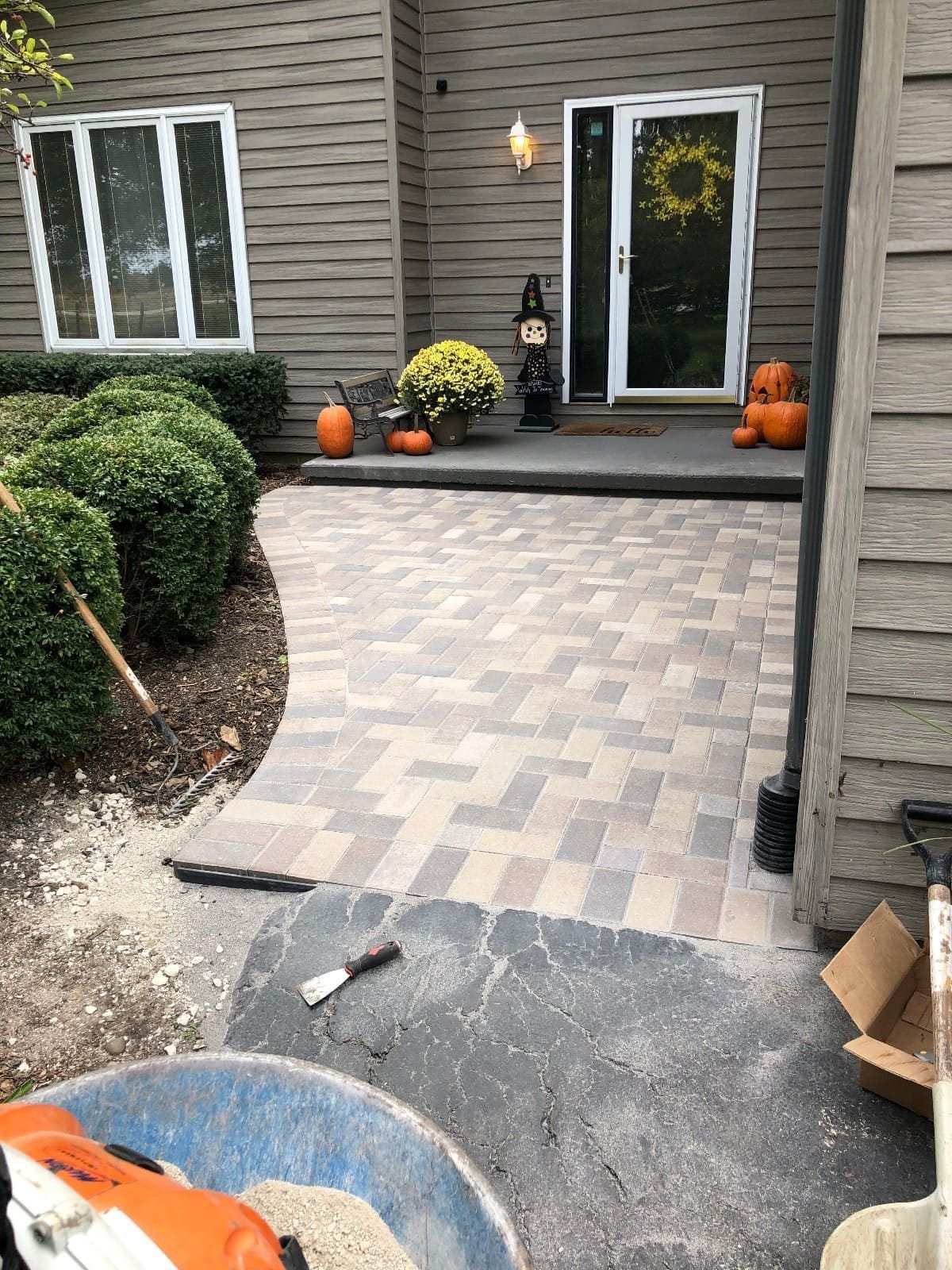 A brick pathway leading to a house entrance decorated with pumpkins and a Halloween wreath.
