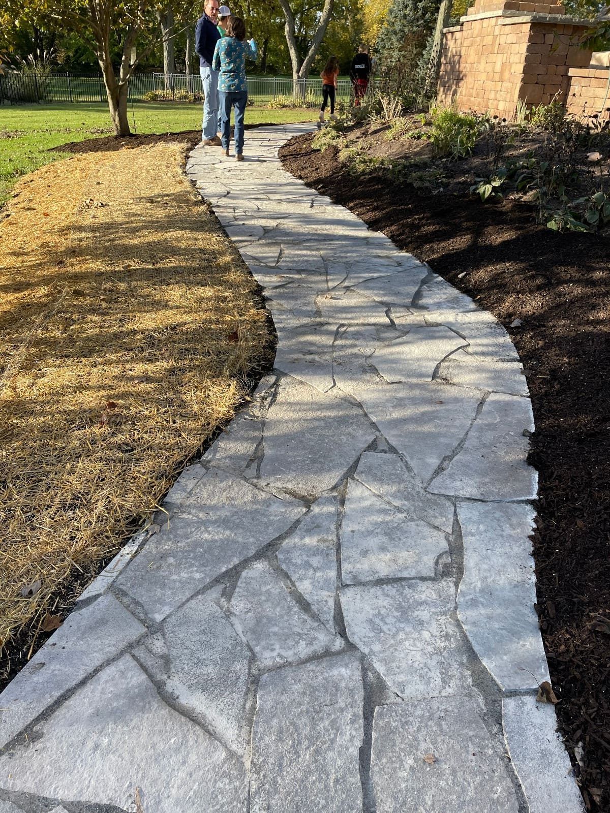 Stone pathway curves through a yard; two people walk on it.