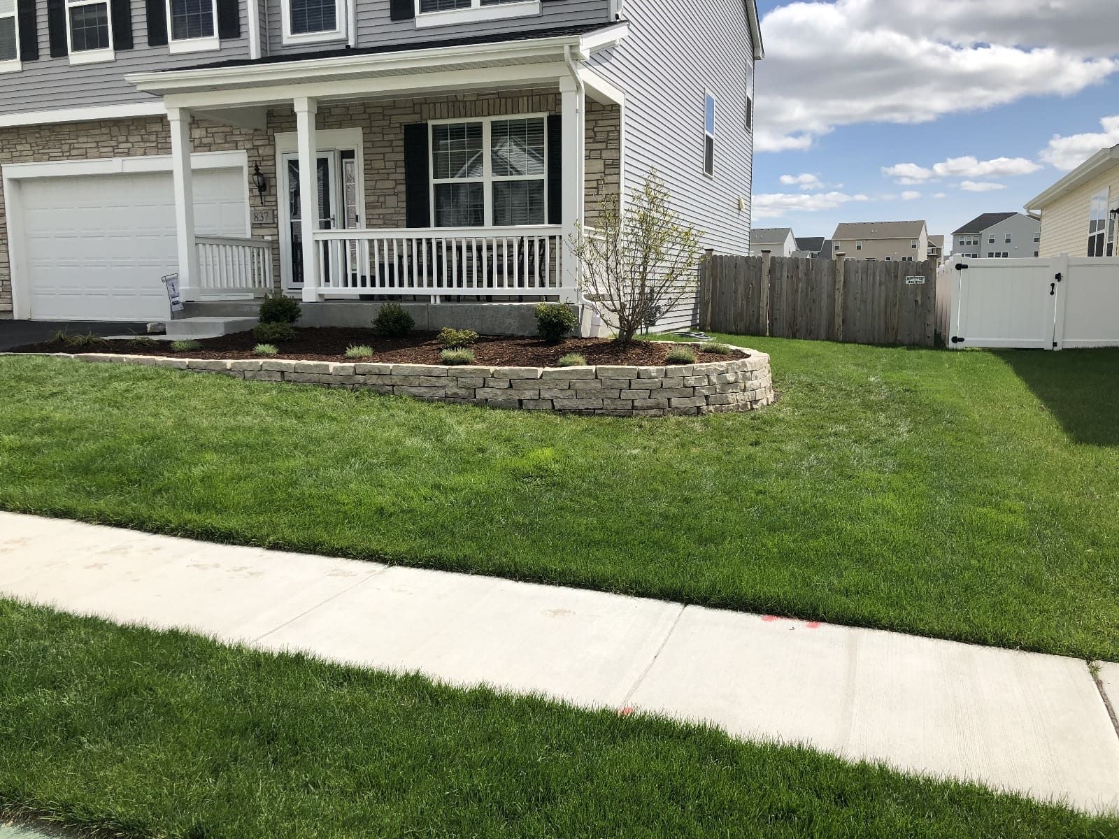 House with a stone-edged flower bed, porch, and a well-manicured lawn on a sunny day.