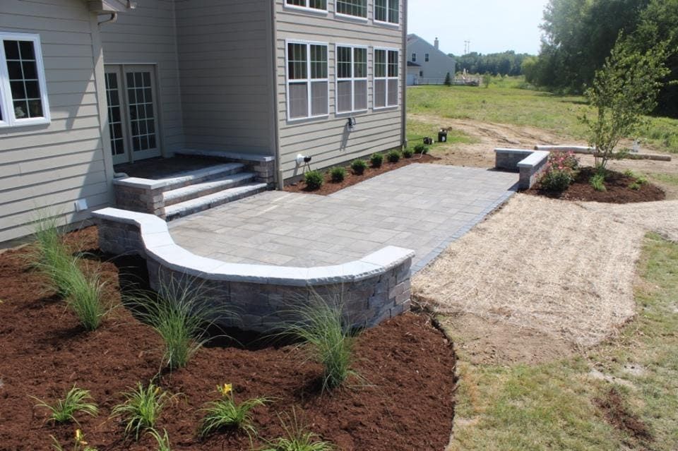 Stone patio with curved retaining wall, steps leading to house entrance, and landscaping.