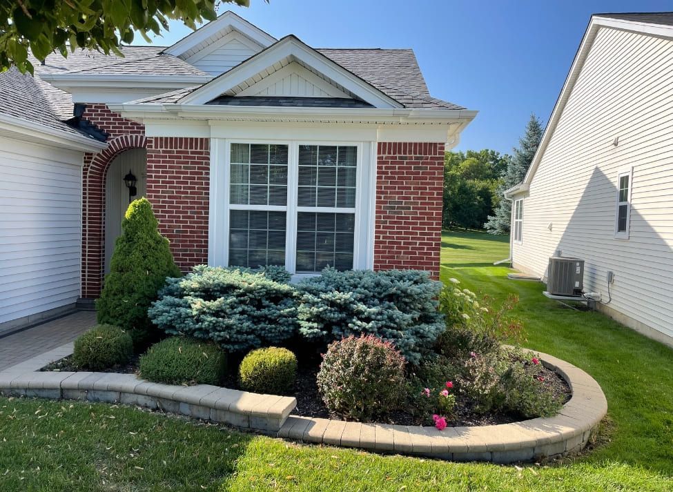 Brick house with manicured landscaping in front, blue and green bushes, and a retaining wall.