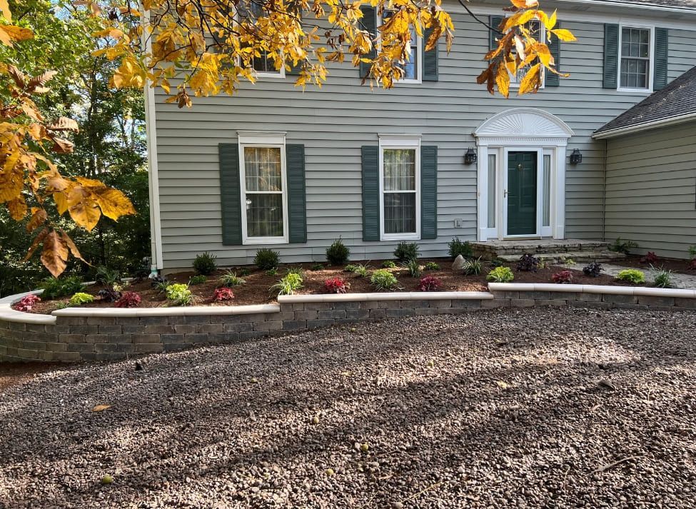 House with green siding and landscaping with a retaining wall, gravel driveway, and autumn leaves.