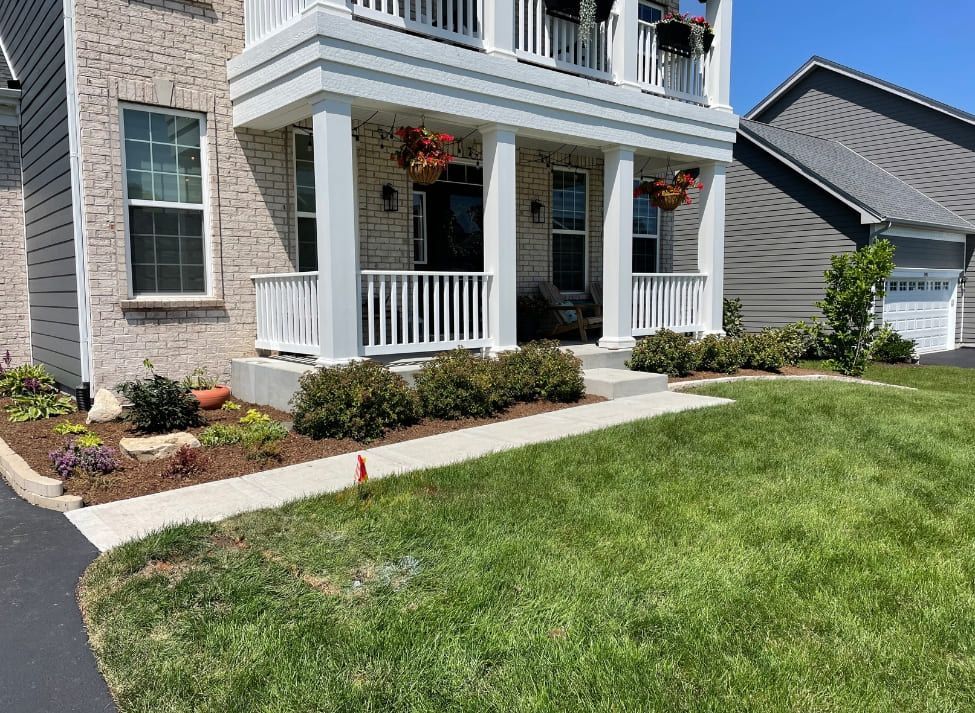 Front exterior of a two-story house with a white porch and landscaping; sunny day.