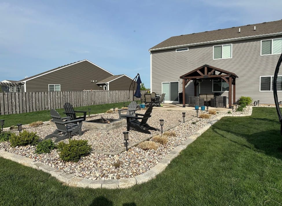 Backyard with a gravel fire pit, seating, and a covered patio next to a two-story house.