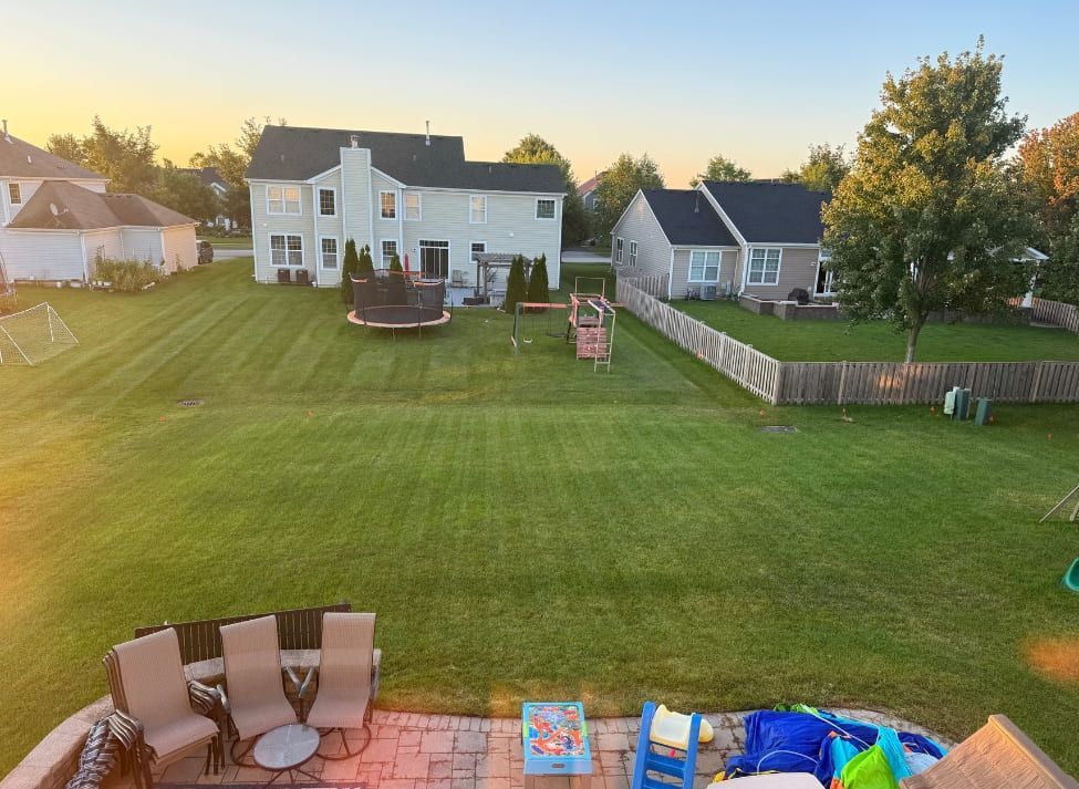 Backyard with houses, green lawn, a trampoline, a playset, and patio furniture.