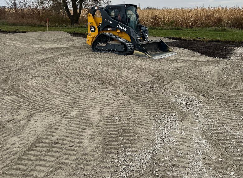 John Deere skid steer on gravel, leveling a work site outdoors.