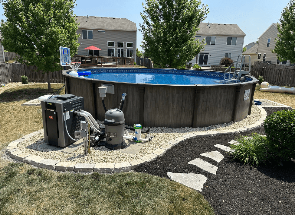 Above-ground pool in a backyard surrounded by landscaping, with equipment visible. Blue water, brown siding.
