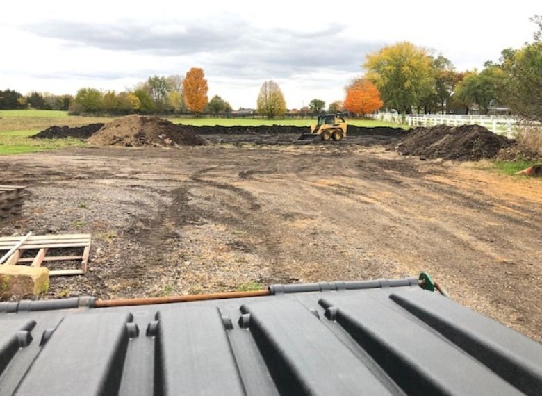 A small construction vehicle leveling dirt in a field, piles of dirt on sides, autumn trees in background.