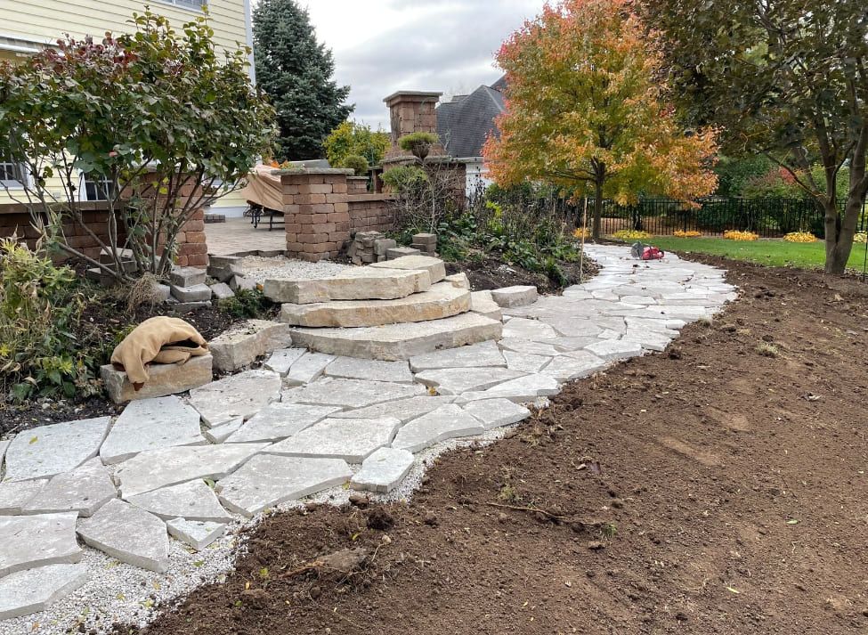 Stone pathway winding through a garden, leading to a brick feature and steps. Autumn foliage in background.