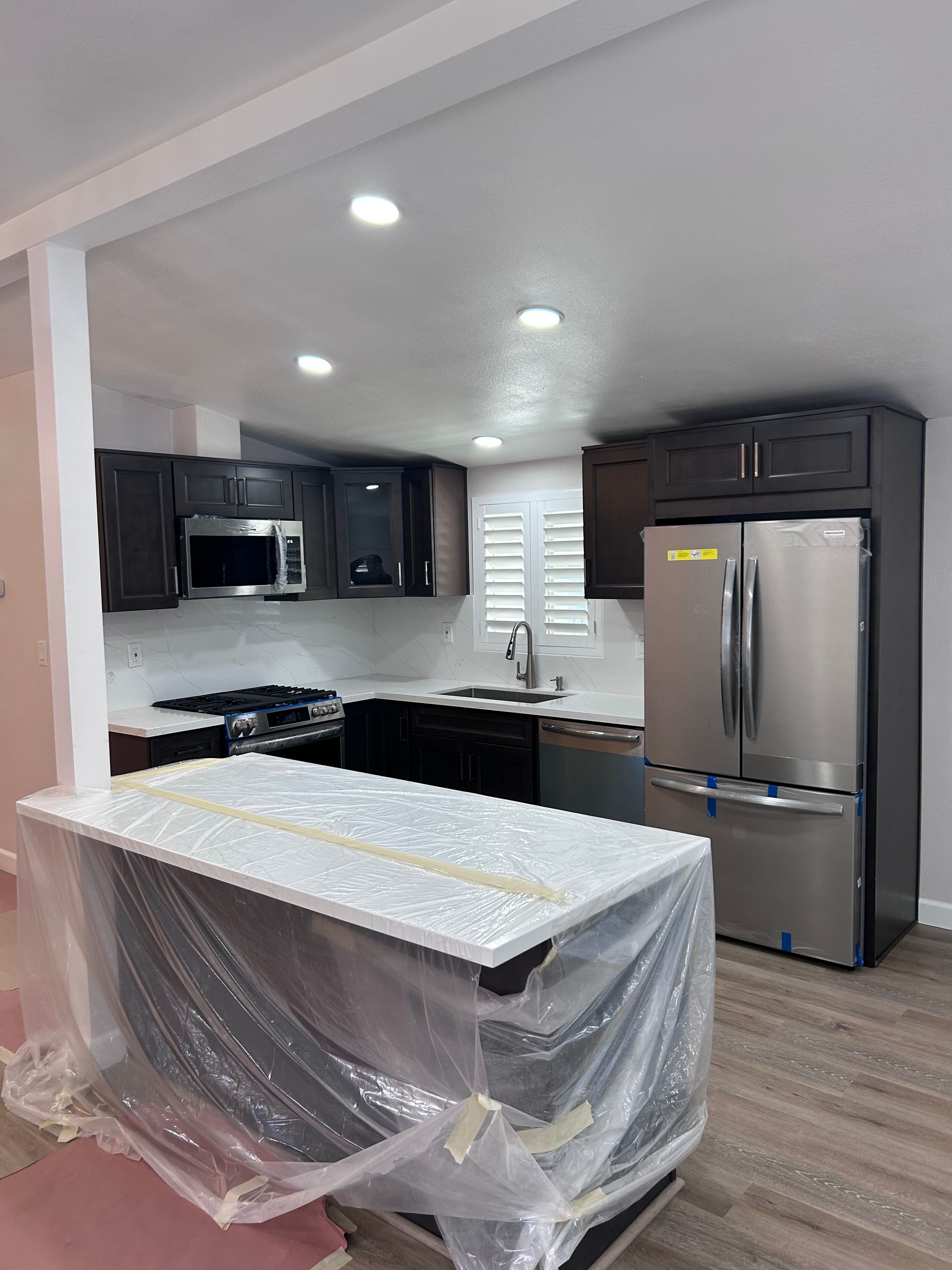 A modern kitchen with dark brown cabinets, a stainless steel refrigerator, and an island covered in protective plastic.