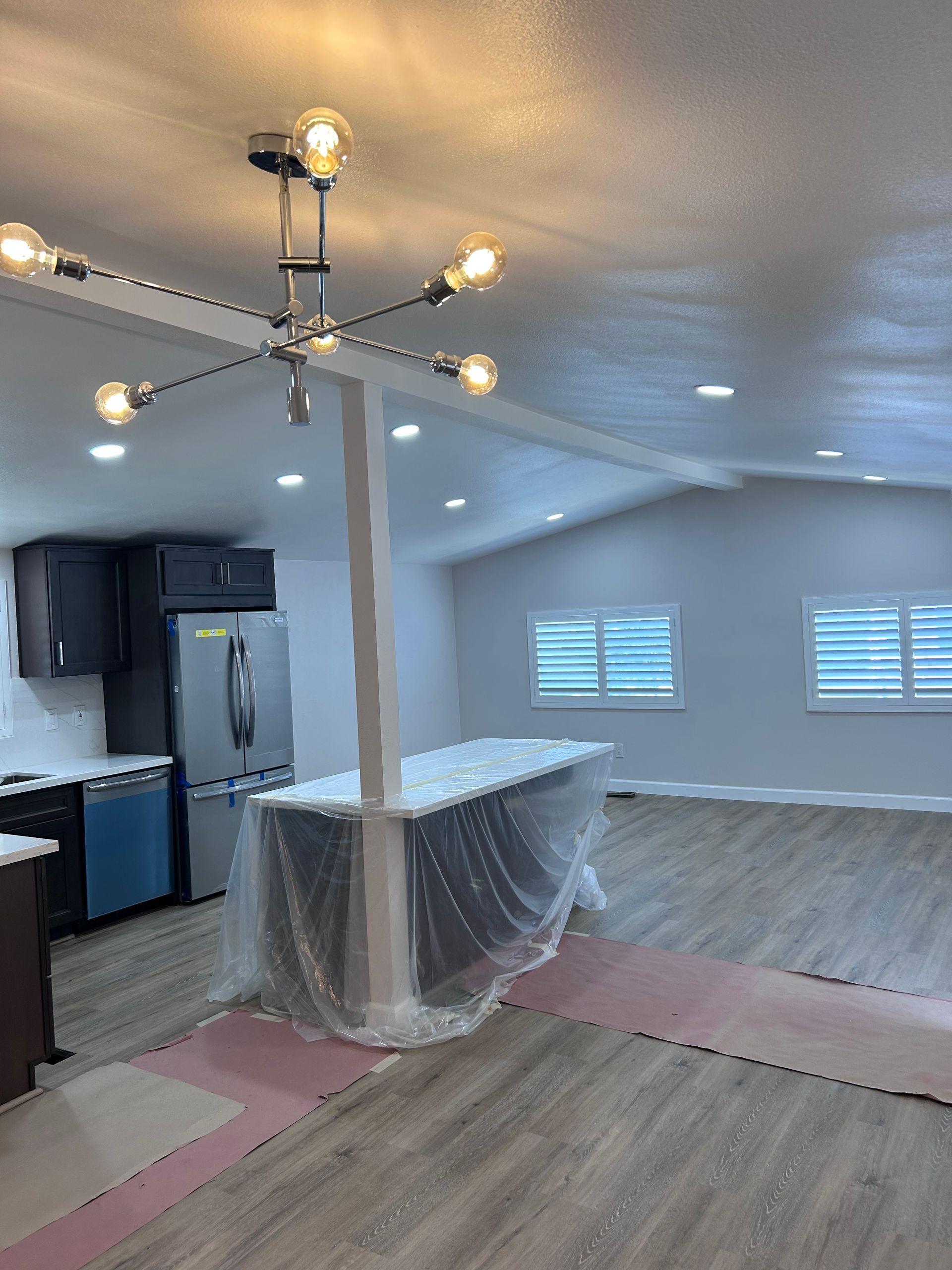 A renovated open-plan kitchen and living space with a modern light fixture, gray cabinets, and light wood-look flooring.