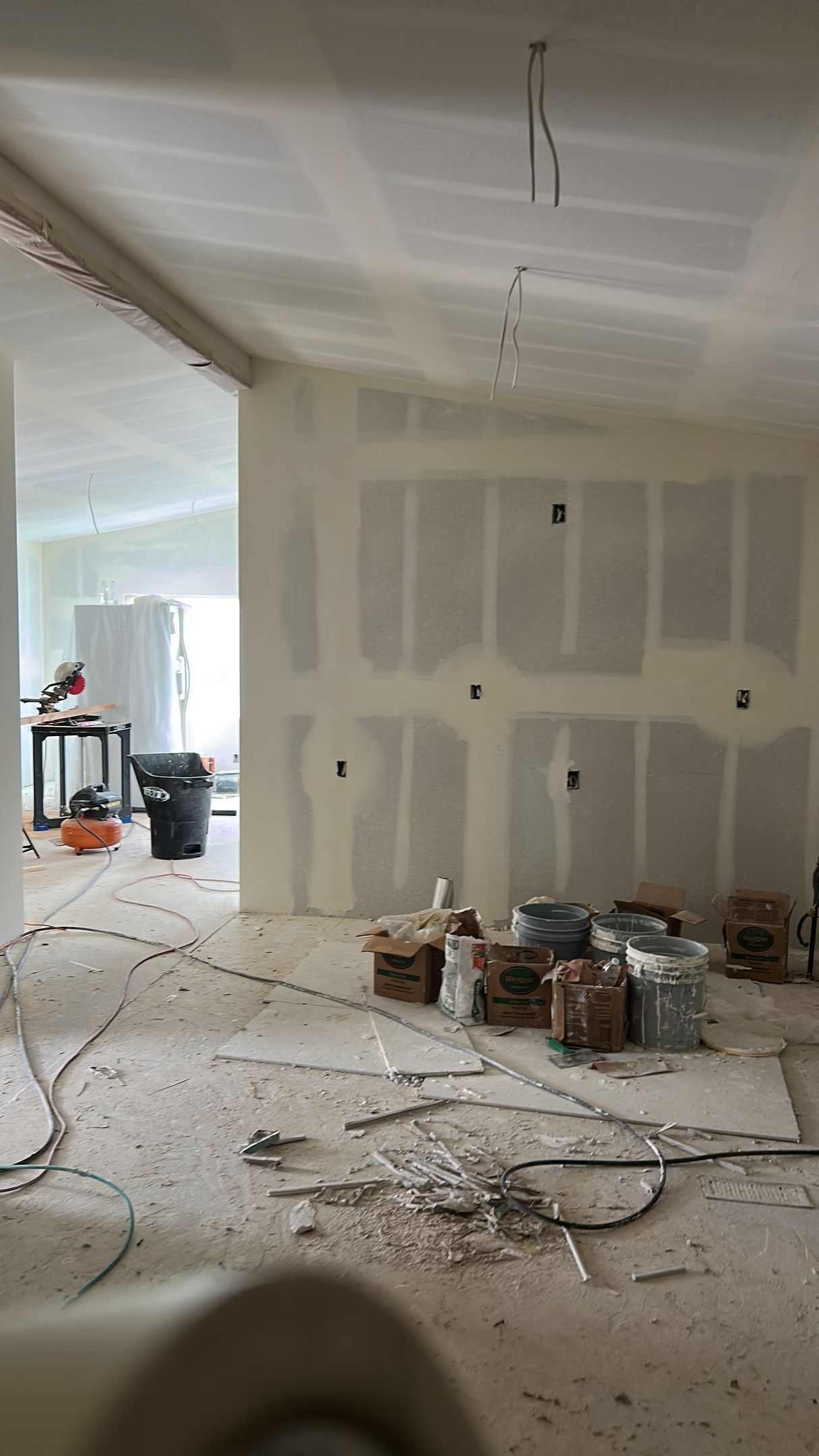 An interior view of a room under construction with unfinished drywall, exposed wiring, and building supplies.