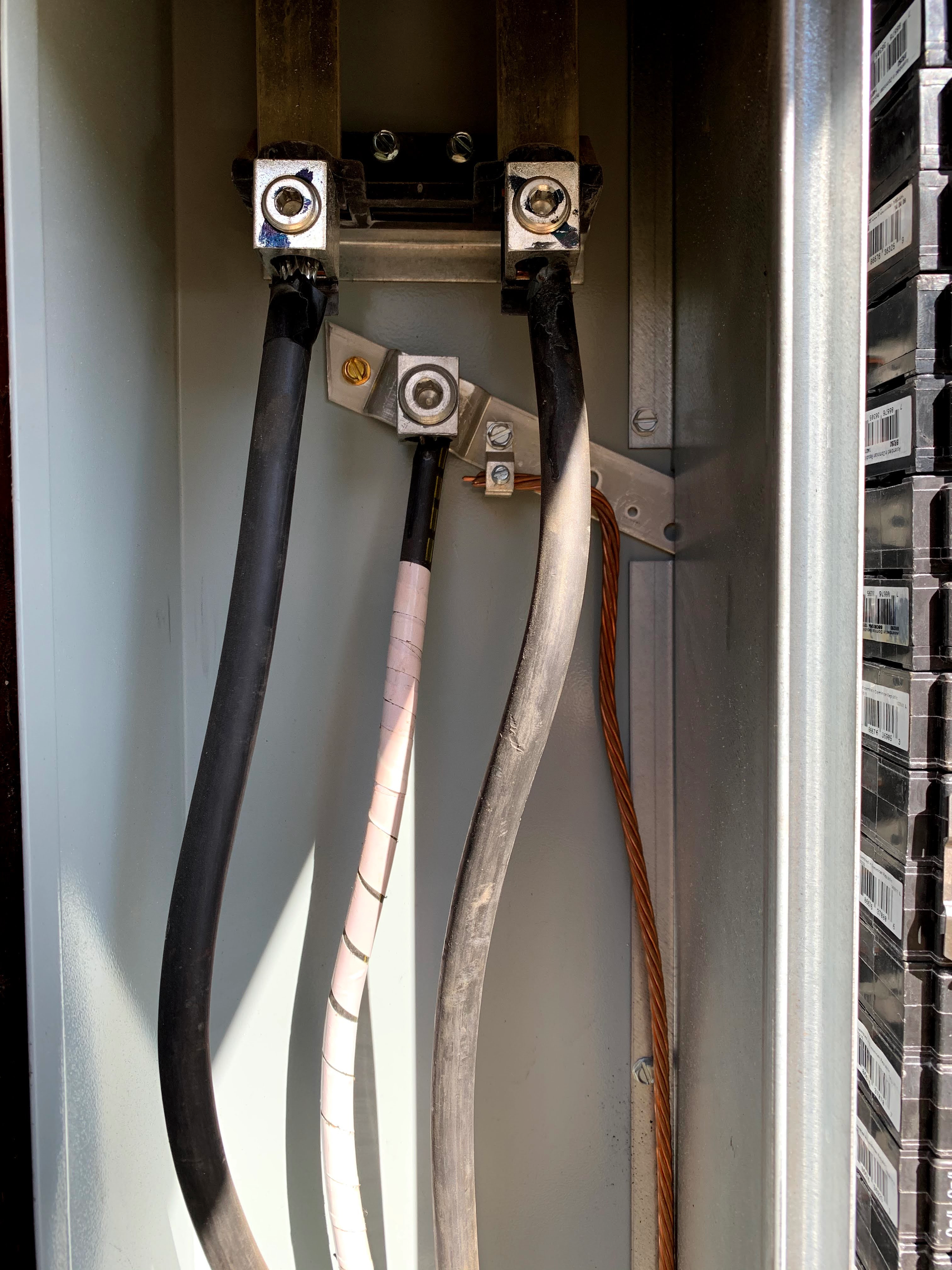 Interior view of an electrical panel showing two main power cables connected to top lugs and a central neutral wire.