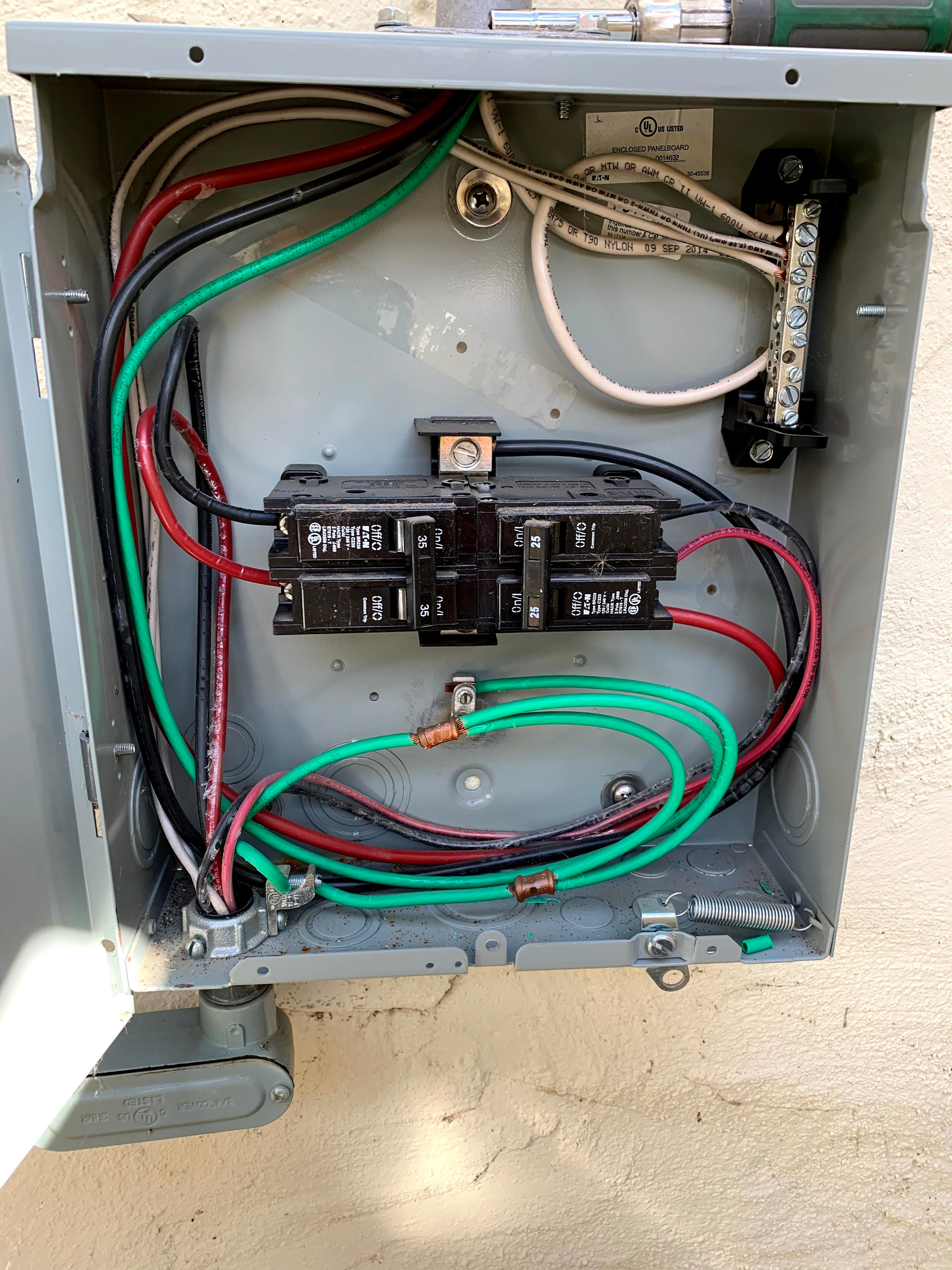 An open electrical service panel showing a main circuit breaker with connected red, black, white, and green wiring.