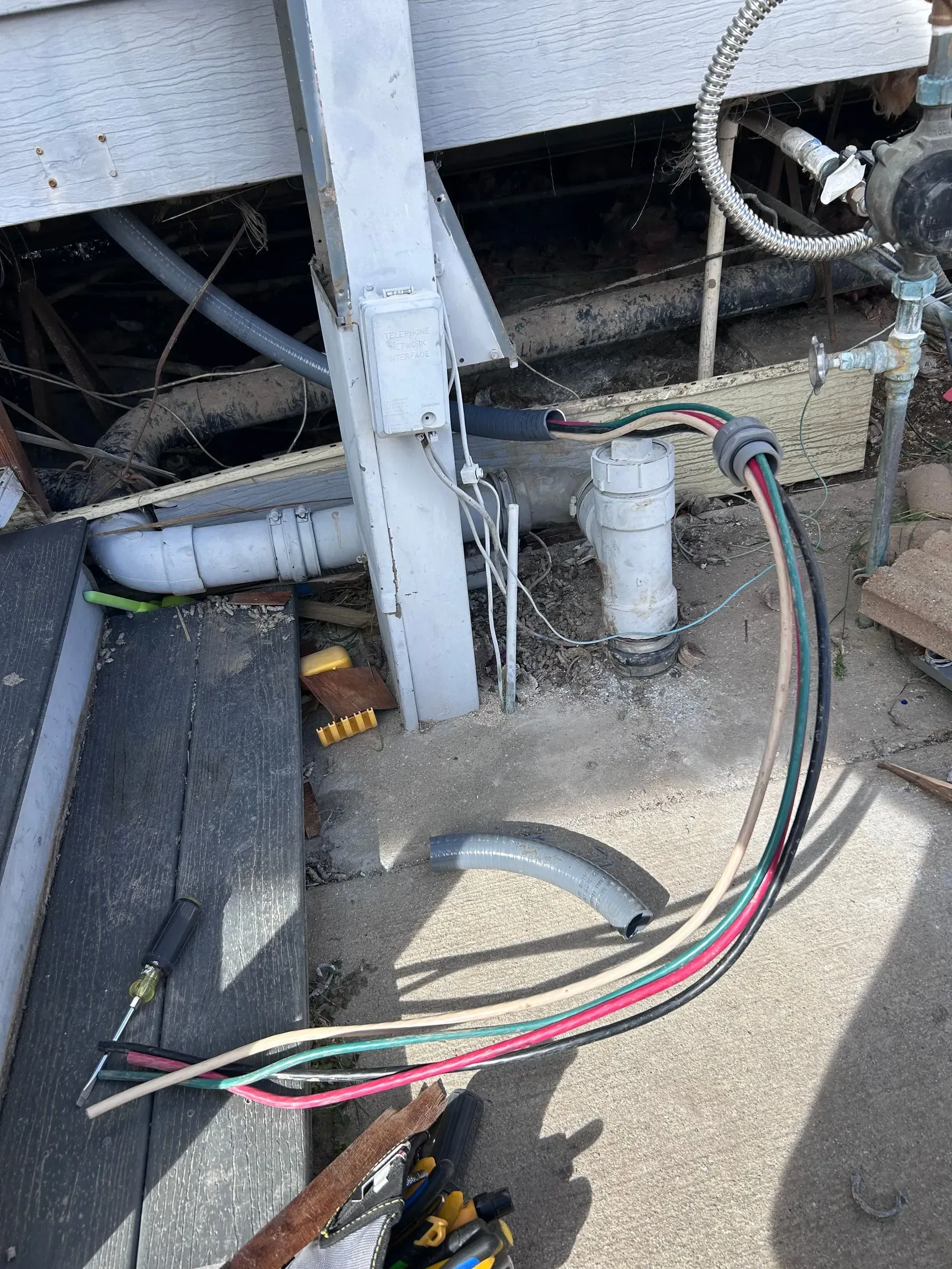 An outdoor view of an electrical wiring project with exposed multi-colored wires extending from a conduit on a post.