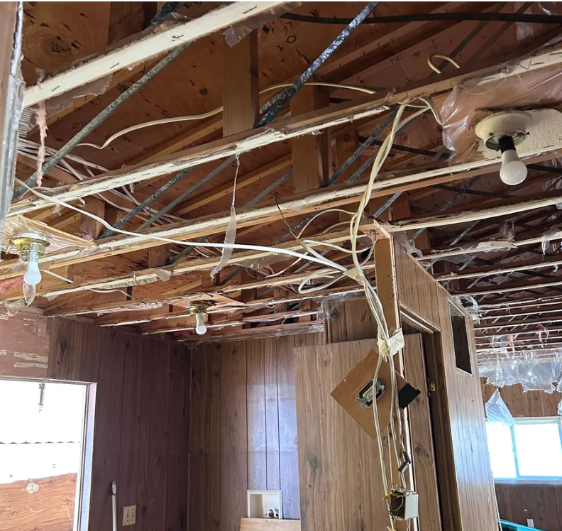 Exposed wood ceiling joists and wiring in a room under renovation, with several bare lightbulbs hanging from the frame.