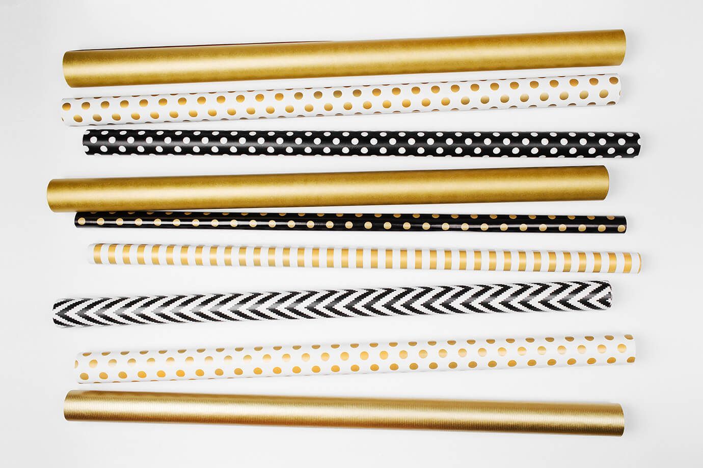 Rolls of wrapping paper in gold, black, and white patterns laid out on a white surface.