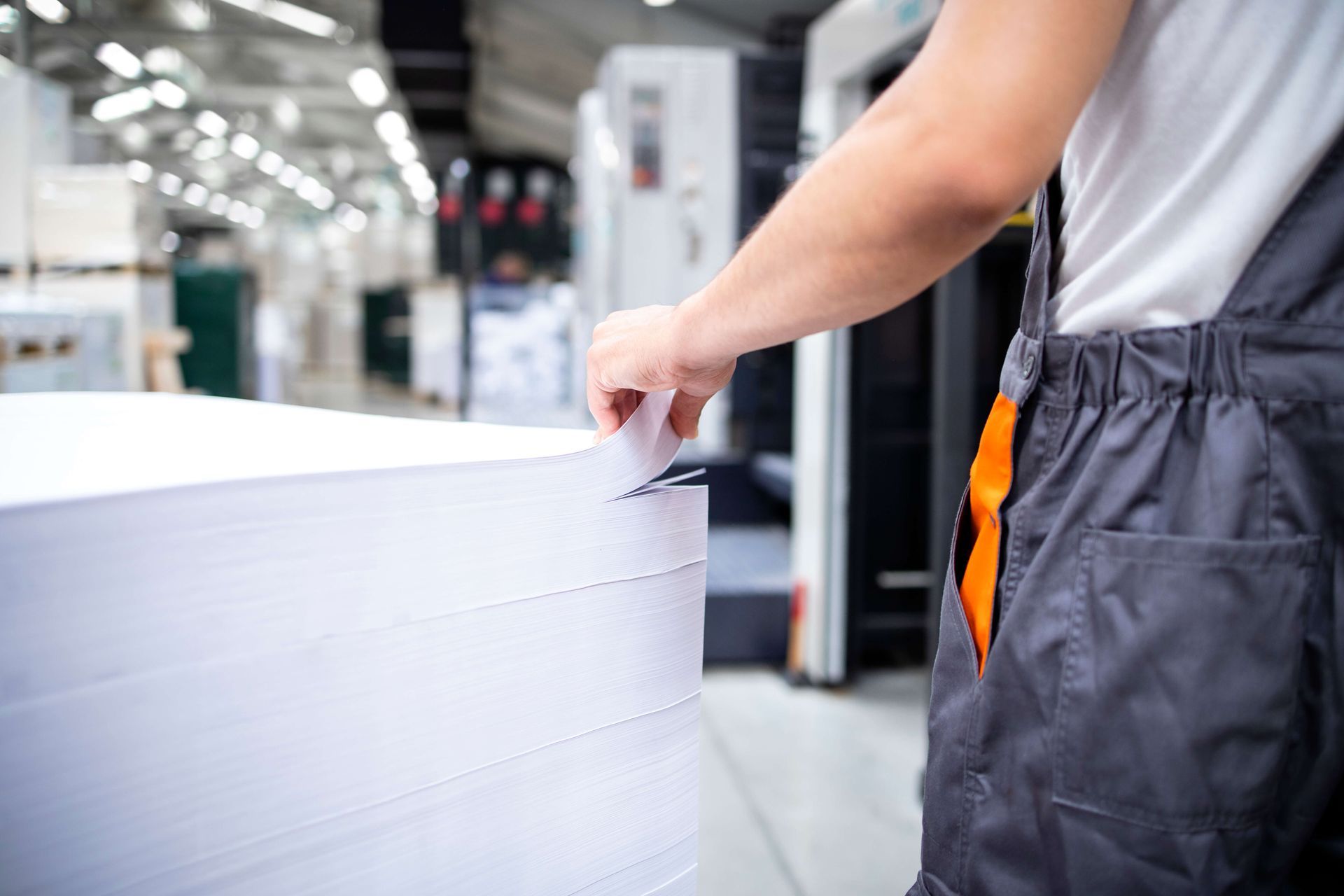 A man is standing next to a large stack of paper in a factory.