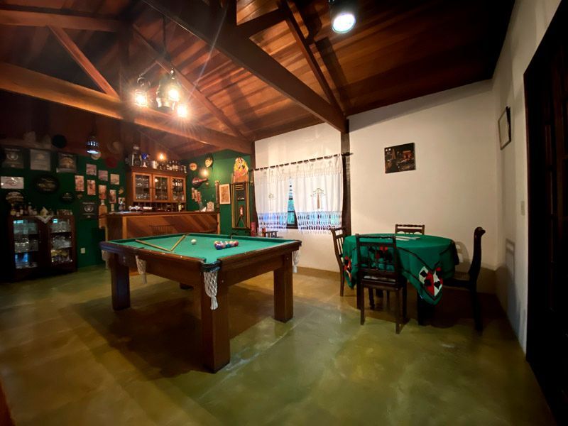 Mesa de bilhar em uma sala com decoração em tons de verde e madeira. Há também uma mesa de jantar na sala.