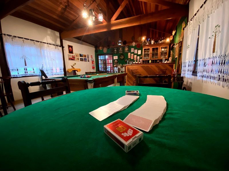 Mesa de cartas com feltro verde, mesa de bilhar e bar em uma sala com painéis de madeira.