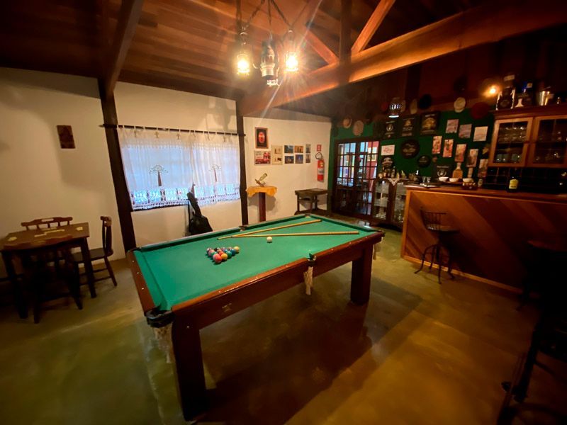 Mesa de bilhar em uma sala com painéis de madeira, bar, cadeiras e prêmios expostos.