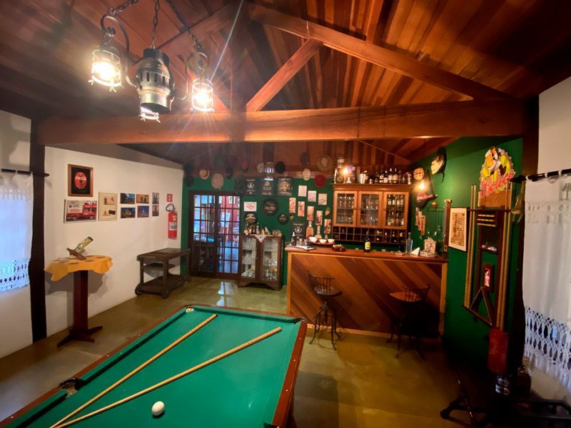 Mesa de bilhar em um bar rústico com detalhes em madeira, paredes verdes e objetos decorativos.