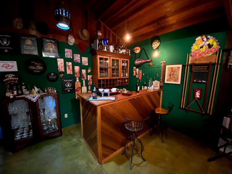 Bar aconchegante em casa com balcão de madeira, prateleiras de bebidas e paredes verdes. Decoração vintage.