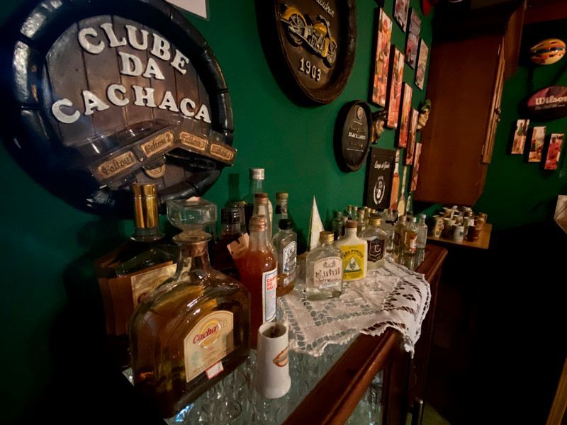 Prateleira de bar com garrafas de bebidas alcoólicas, uma placa que diz
