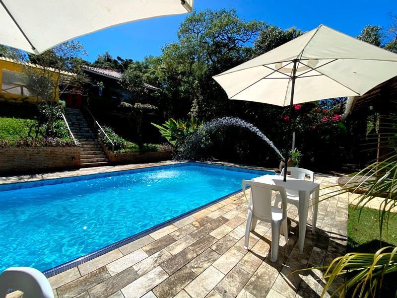 Piscina com fonte, mobiliário de jardim e guarda-sóis num dia ensolarado.