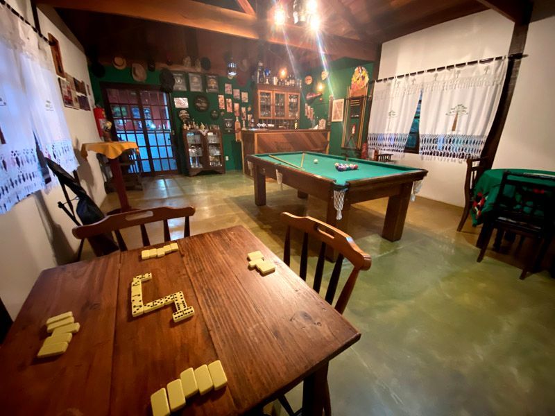 Sala de jogos com mesa de bilhar, mesa de dominó, cadeiras e decoração nas paredes.