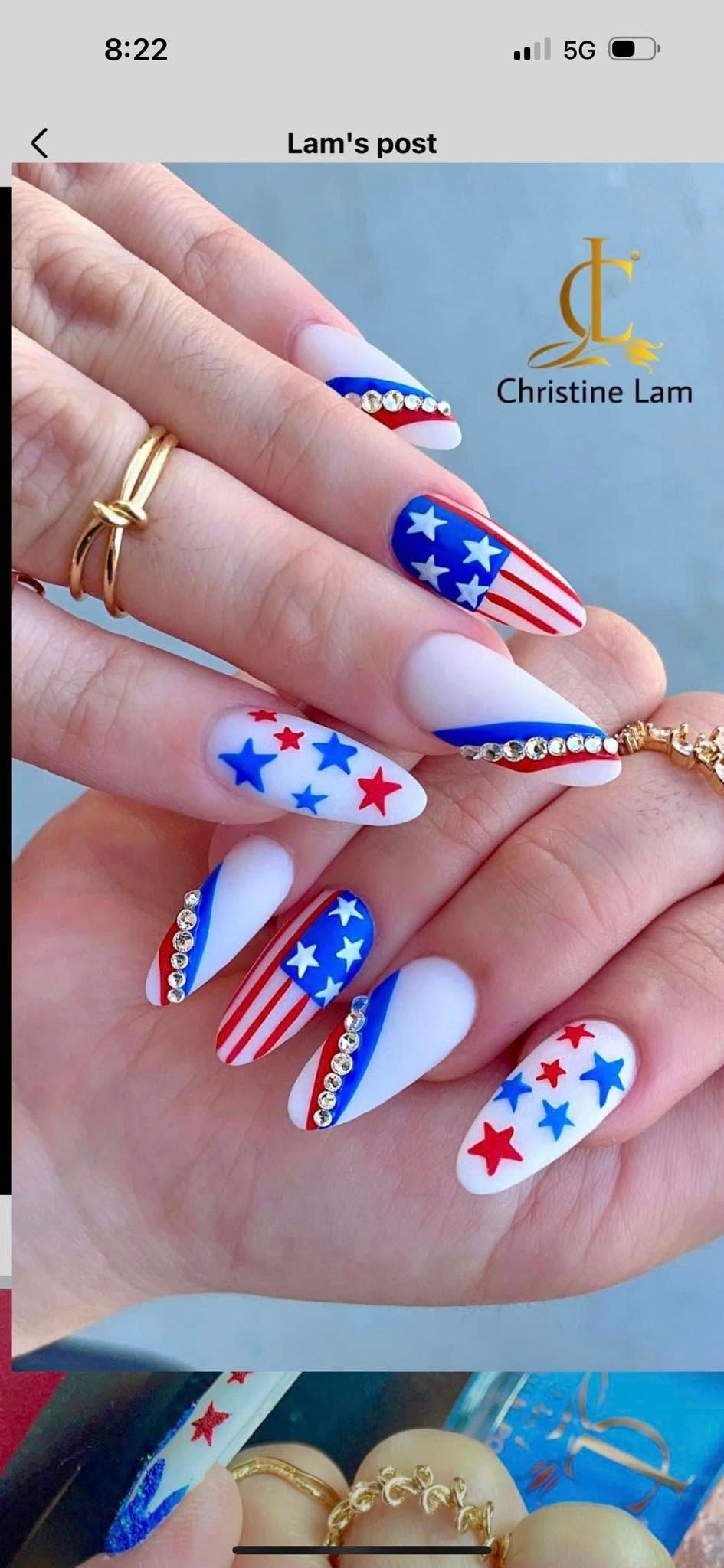 Hands showing long, almond-shaped nails with American flag patterns, blue and red stars, and white base polish.